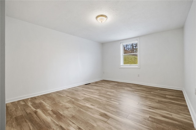 empty room with a textured ceiling, baseboards, and wood finished floors