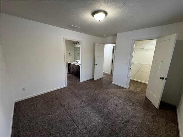 unfurnished bedroom with sink, connected bathroom, a textured ceiling, dark carpet, and a walk in closet