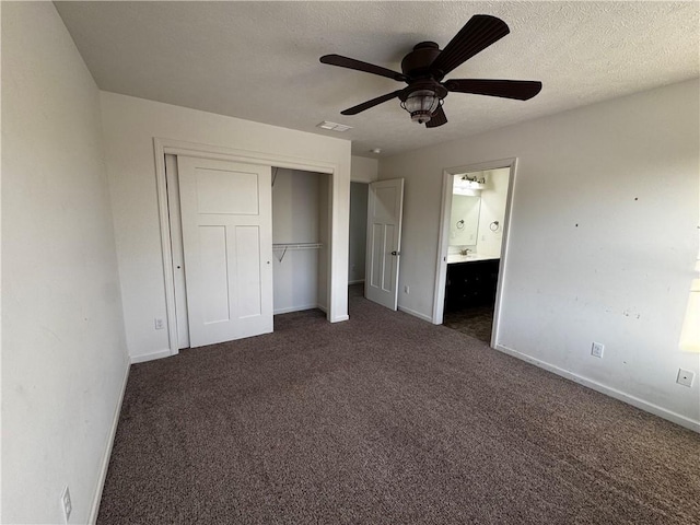 unfurnished bedroom featuring ceiling fan, ensuite bathroom, a textured ceiling, dark carpet, and a closet