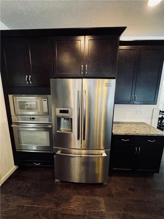 kitchen with light stone counters, stainless steel appliances, dark hardwood / wood-style flooring, and a textured ceiling