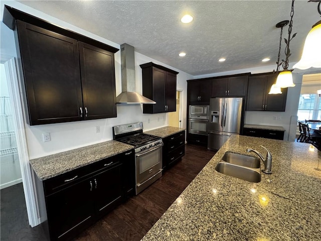 kitchen featuring sink, dark brown cabinets, hanging light fixtures, stainless steel appliances, and wall chimney range hood