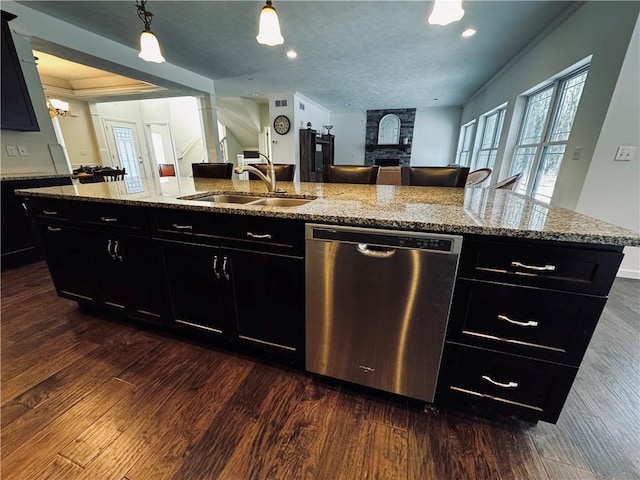 kitchen with a kitchen island with sink, sink, light stone counters, and stainless steel dishwasher