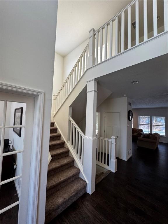 stairs with wood-type flooring, decorative columns, and a high ceiling