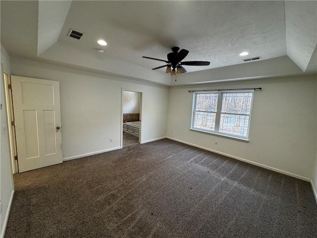 unfurnished bedroom with ceiling fan, ensuite bathroom, a tray ceiling, and dark colored carpet