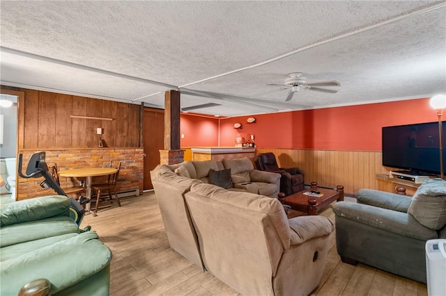 living room with ceiling fan, wood walls, a textured ceiling, and light hardwood / wood-style flooring