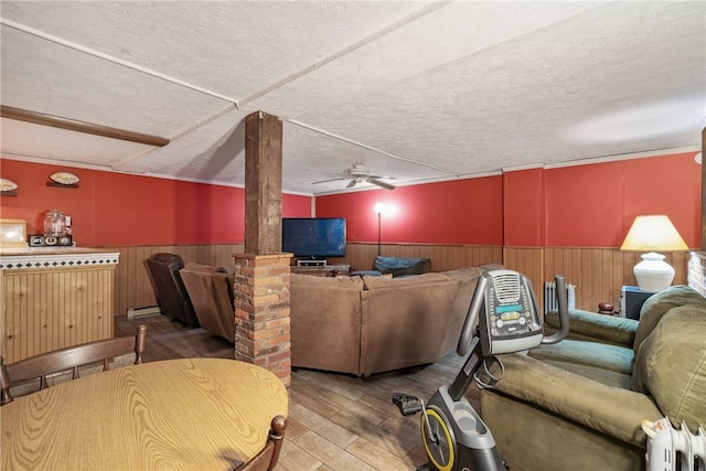 living room featuring ceiling fan, a baseboard heating unit, decorative columns, a textured ceiling, and light wood-type flooring