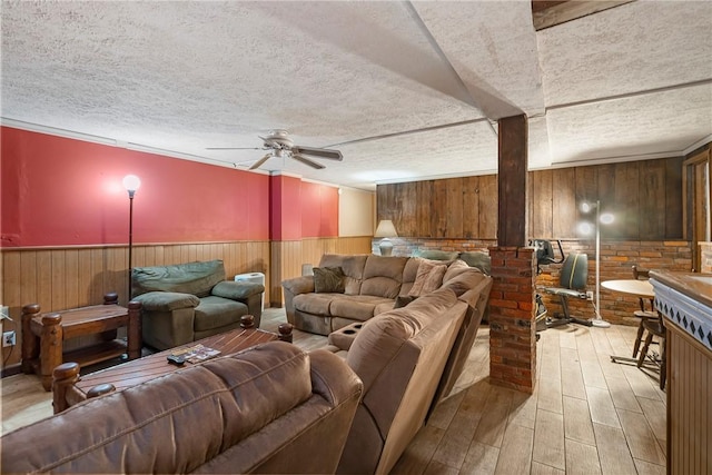 living room with ceiling fan, light hardwood / wood-style floors, a textured ceiling, and wood walls