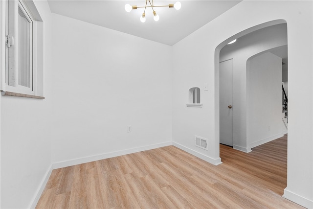 unfurnished room with a notable chandelier and light wood-type flooring