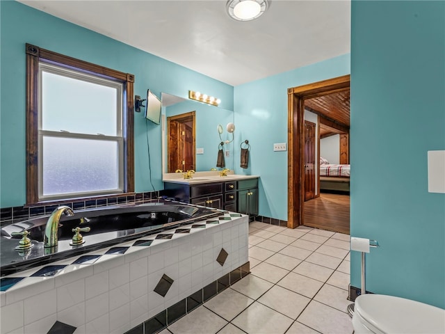 bathroom featuring tile patterned flooring, vanity, a relaxing tiled tub, and toilet