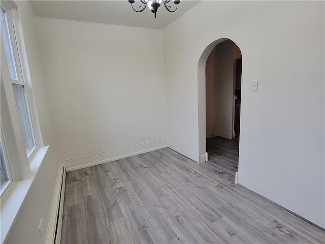 empty room featuring a notable chandelier, light hardwood / wood-style flooring, and a baseboard heating unit