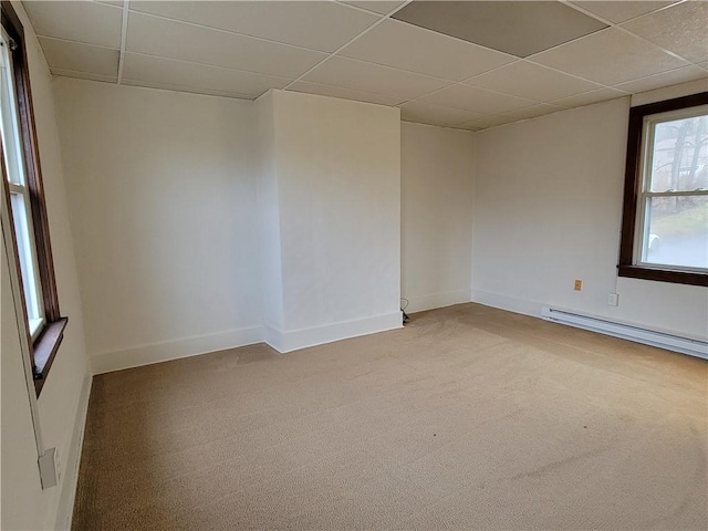 spare room featuring a baseboard heating unit, light carpet, and a drop ceiling