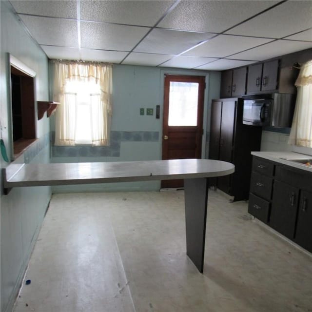 kitchen with black appliances, dark brown cabinets, a drop ceiling, and kitchen peninsula