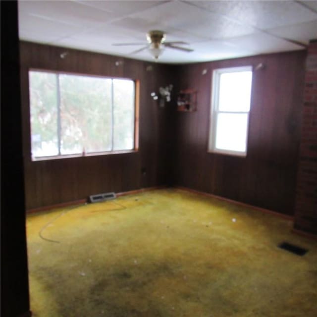 carpeted spare room featuring ceiling fan and wood walls