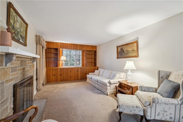 carpeted living room with built in shelves, a stone fireplace, and wood walls