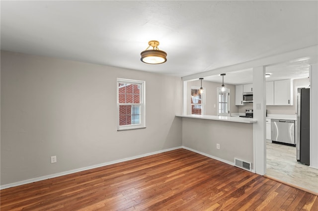 interior space featuring appliances with stainless steel finishes, white cabinets, hardwood / wood-style flooring, hanging light fixtures, and kitchen peninsula