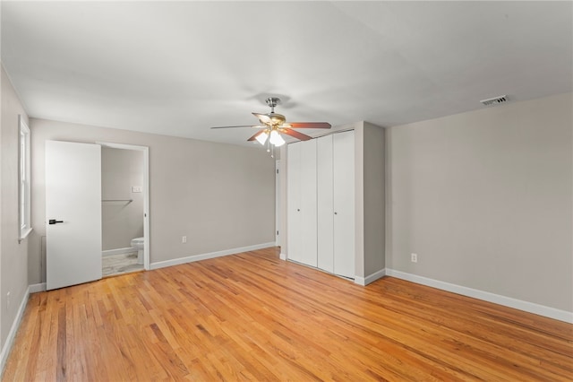 unfurnished bedroom with ceiling fan, a closet, light wood-type flooring, and ensuite bath