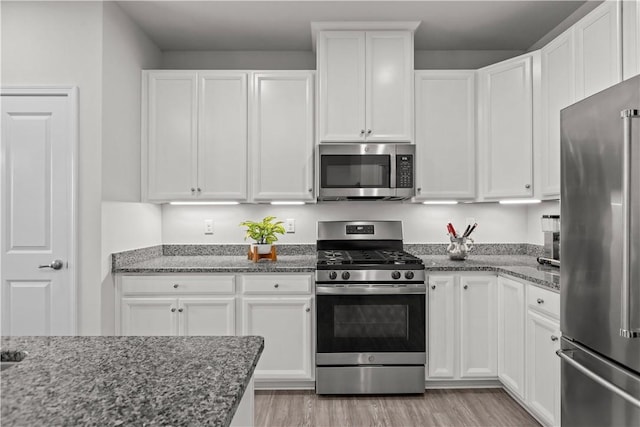 kitchen featuring white cabinetry, appliances with stainless steel finishes, light hardwood / wood-style floors, and dark stone counters