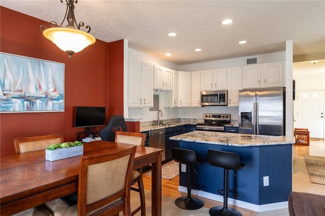 kitchen with light stone counters, decorative light fixtures, a center island, stainless steel appliances, and white cabinets