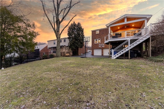 back house at dusk with a garage, a wooden deck, ceiling fan, and a lawn