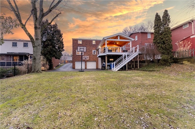 back house at dusk with a wooden deck, a garage, and a lawn