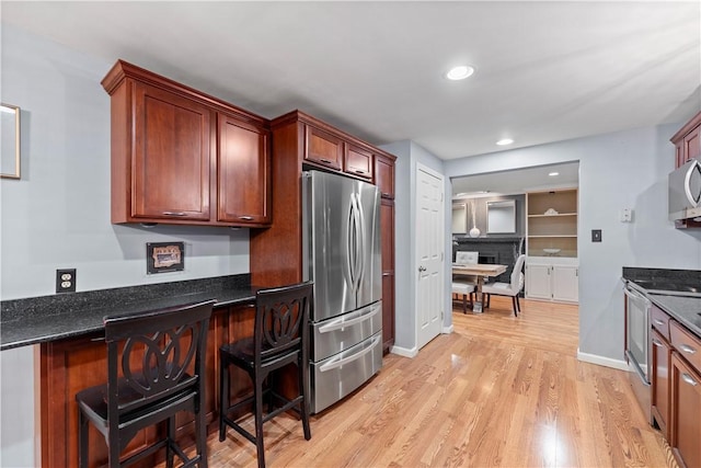 kitchen with appliances with stainless steel finishes, light hardwood / wood-style floors, and dark stone countertops