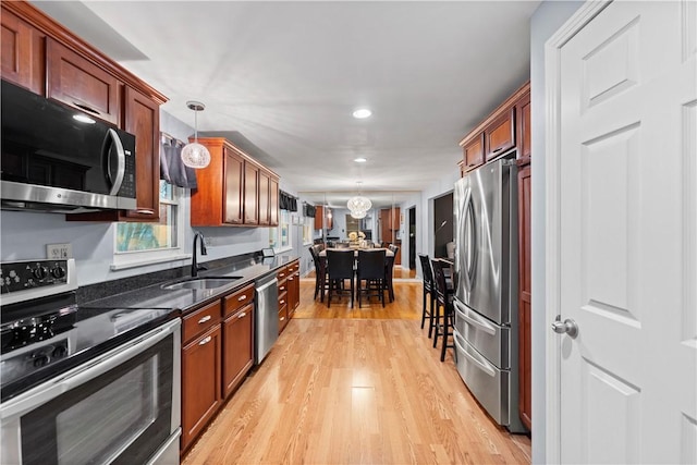 kitchen with sink, hanging light fixtures, dark stone countertops, light hardwood / wood-style flooring, and stainless steel appliances