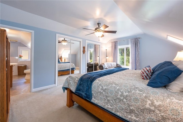 bedroom featuring ensuite bath, vaulted ceiling, light carpet, two closets, and ceiling fan