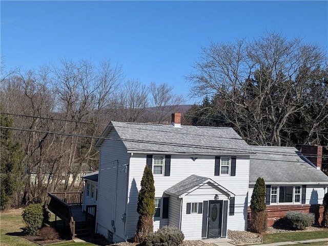 view of front of property with a deck, a front lawn, a chimney, and a shingled roof