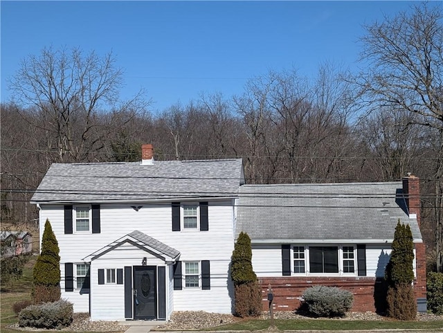 view of front of home with a shingled roof, brick siding, and a chimney