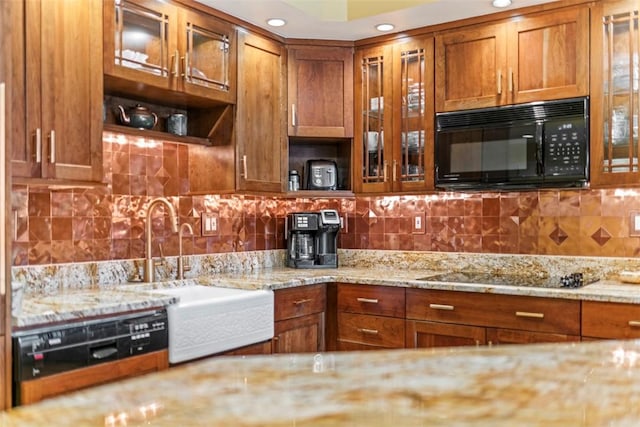 kitchen featuring black appliances, glass insert cabinets, a sink, backsplash, and brown cabinets