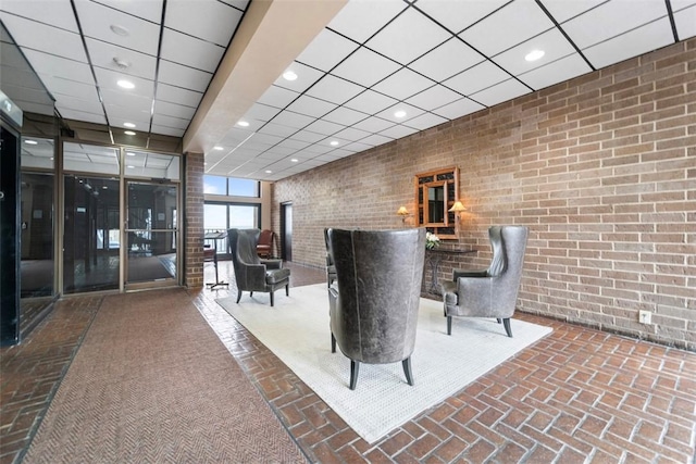 lobby with brick wall, a drop ceiling, and recessed lighting