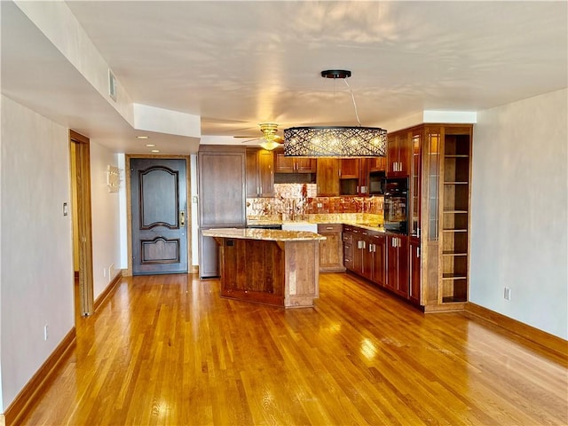 kitchen with dark wood-style floors, decorative backsplash, a kitchen island, light stone counters, and a ceiling fan