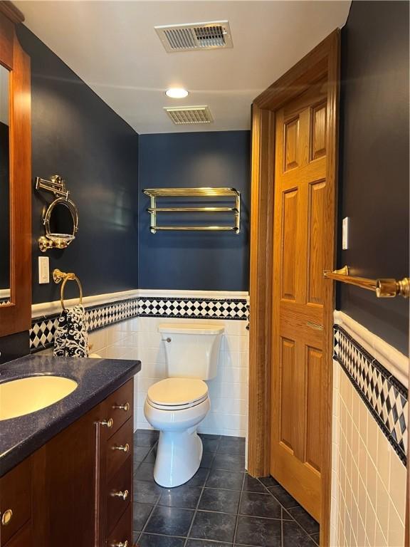 bathroom featuring tile patterned floors, toilet, tile walls, vanity, and a wainscoted wall