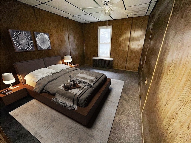 bedroom with a paneled ceiling, dark carpet, and wood walls