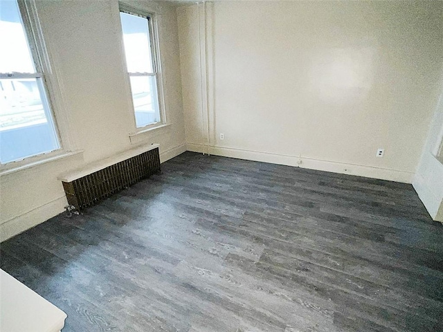 spare room featuring dark wood-type flooring, radiator heating unit, and a wealth of natural light