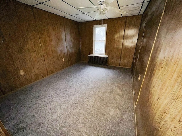 carpeted spare room featuring ceiling fan, a drop ceiling, and wooden walls