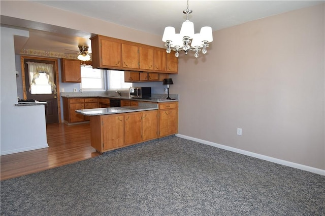 kitchen featuring pendant lighting, sink, dark carpet, ceiling fan with notable chandelier, and kitchen peninsula