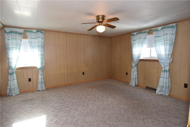 empty room featuring ceiling fan, light carpet, and wooden walls