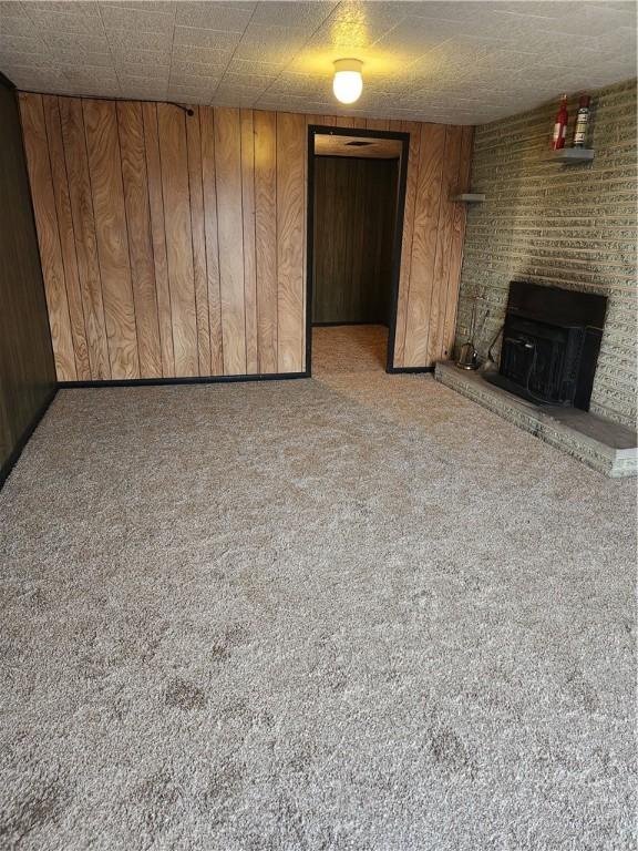 unfurnished living room with a brick fireplace, light colored carpet, and wood walls