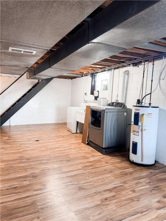 basement featuring water heater, light wood-type flooring, and washer and clothes dryer