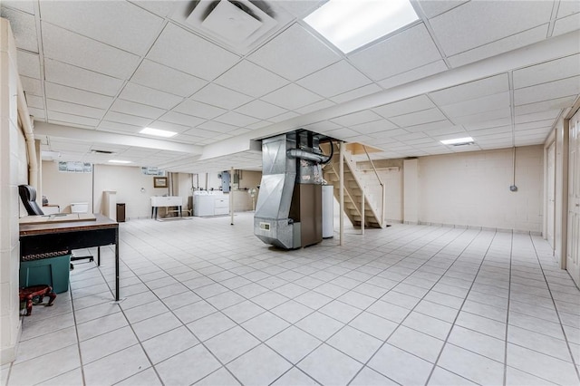 basement featuring heating unit, light tile patterned floors, and a paneled ceiling