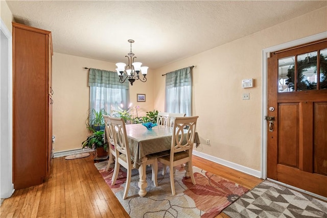 dining space with a notable chandelier, light hardwood / wood-style flooring, a textured ceiling, and a baseboard heating unit