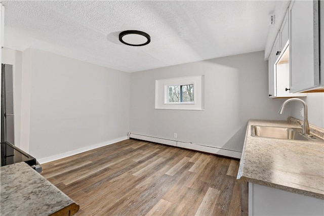 kitchen featuring sink, white cabinetry, wood-type flooring, a textured ceiling, and a baseboard heating unit