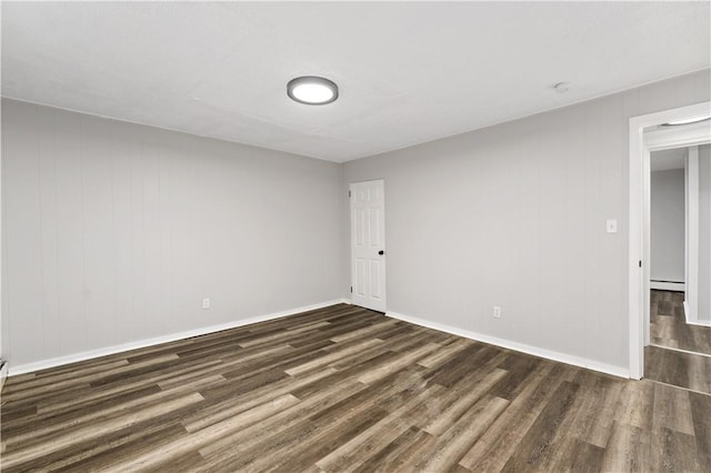 empty room with dark hardwood / wood-style flooring and a baseboard heating unit