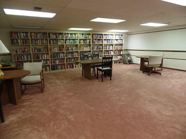 sitting room featuring wall of books, a drop ceiling, and carpet flooring