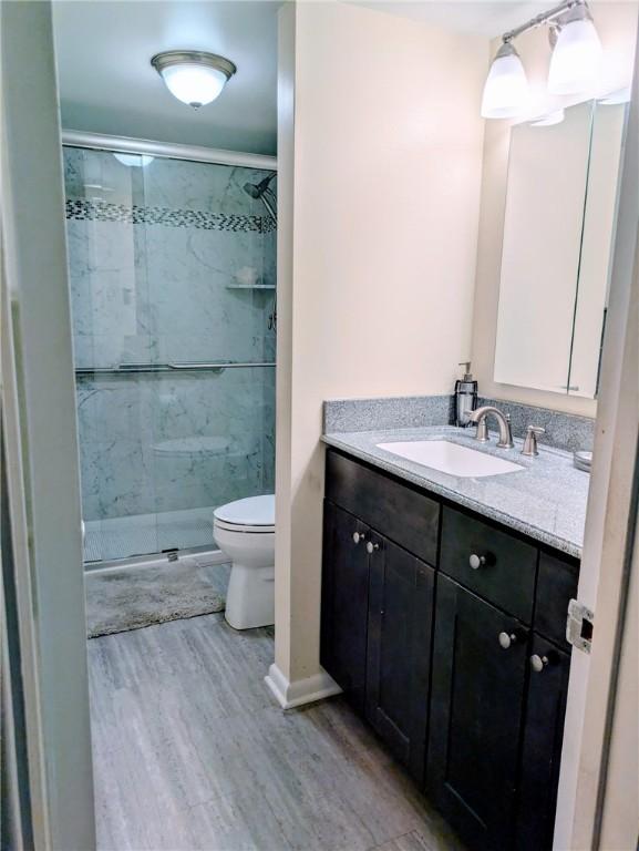 bathroom featuring wood finished floors, toilet, vanity, and a stall shower