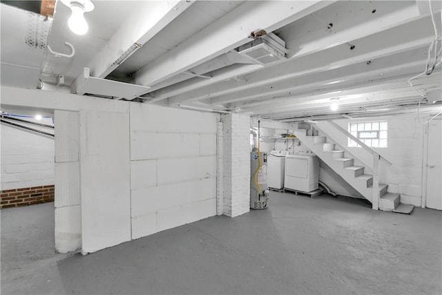 basement featuring water heater, washing machine and clothes dryer, and brick wall