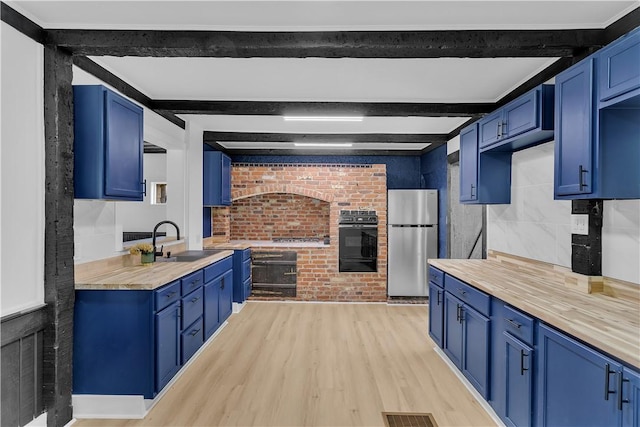 kitchen featuring blue cabinets, sink, stainless steel fridge, light hardwood / wood-style floors, and beam ceiling