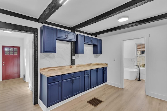 kitchen with beamed ceiling, blue cabinetry, butcher block counters, and light hardwood / wood-style floors