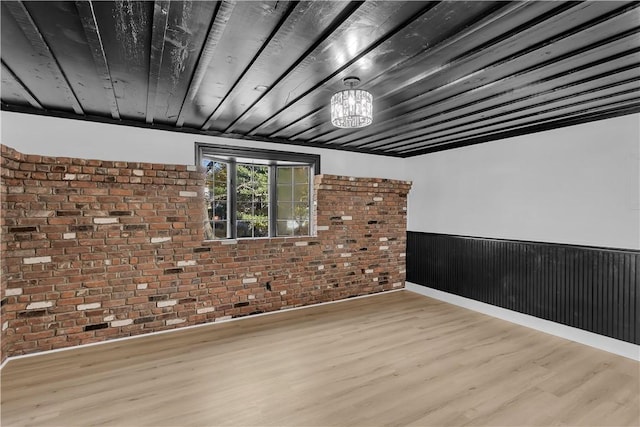 spare room featuring brick wall, wood ceiling, and light wood-type flooring